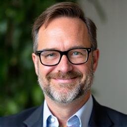 Professional headshot of David Lee, a friendly man with glasses and a neatly trimmed beard, exuding wisdom and experience, wearing a collared shirt.